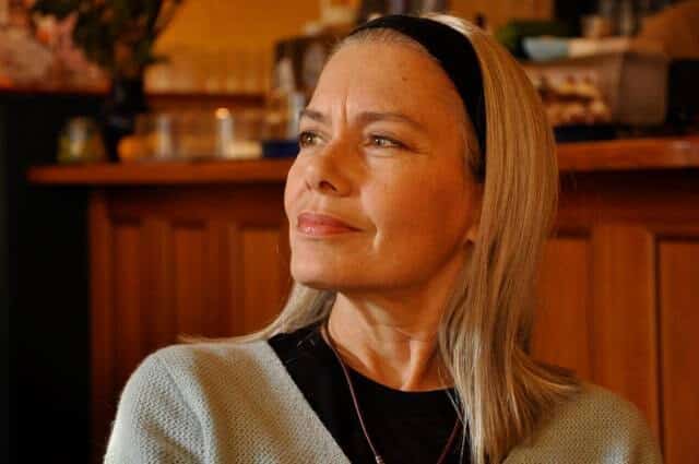 Candida Royalle mit blondem Haar und schwarzem Haarreif, nachdenklich und lächelnd in einem Café